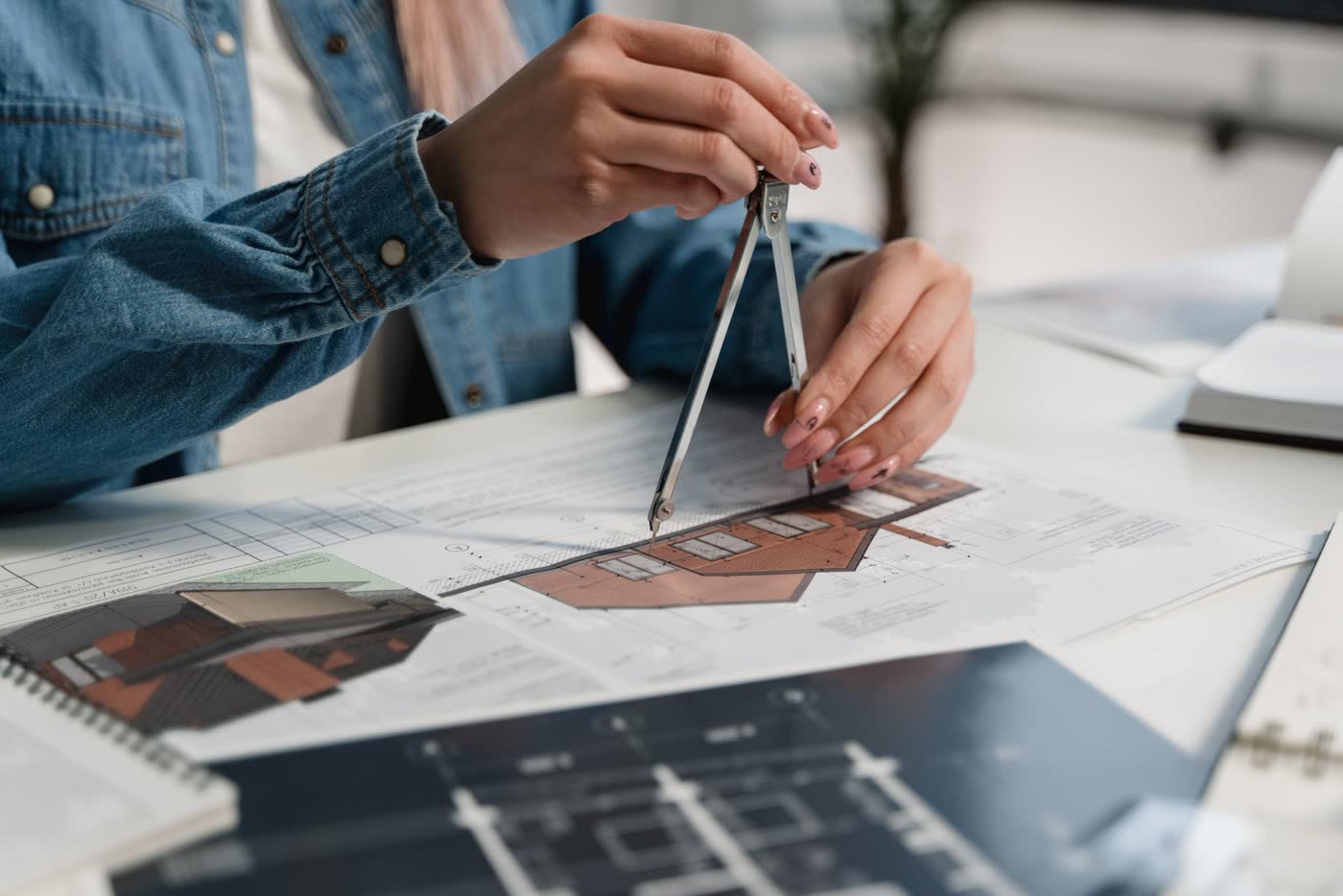 Manos trabajando con compás sobre planos de arquitectura